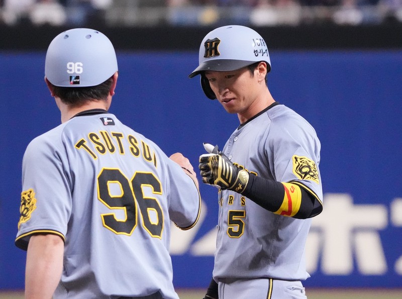 一塁ベース上でタッチを交わす近本(右)と筒井コーチ