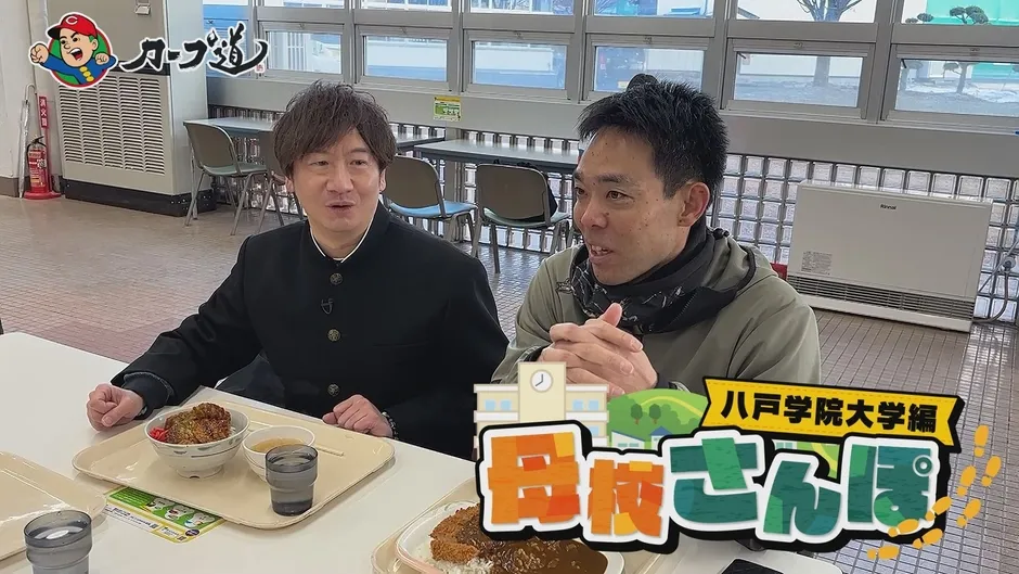 2人の男性が学食のような場所で食事をしながら話をしている様子。